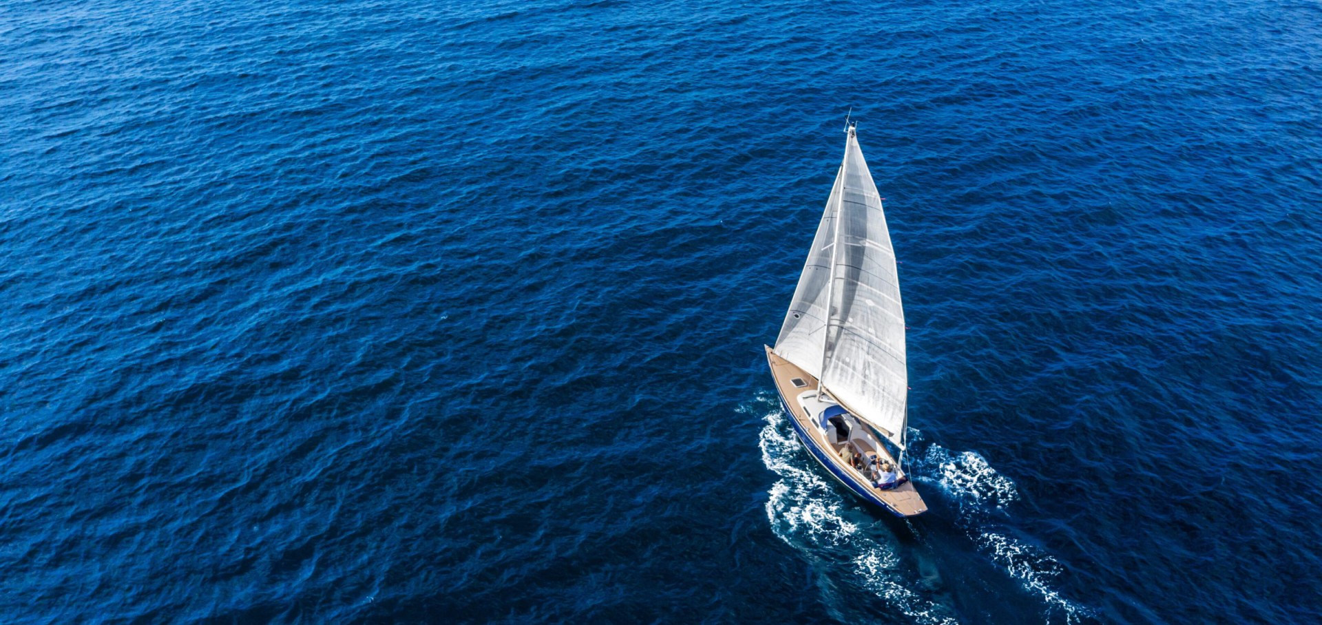 A sailboat gliding on deep blue water under clear skies.