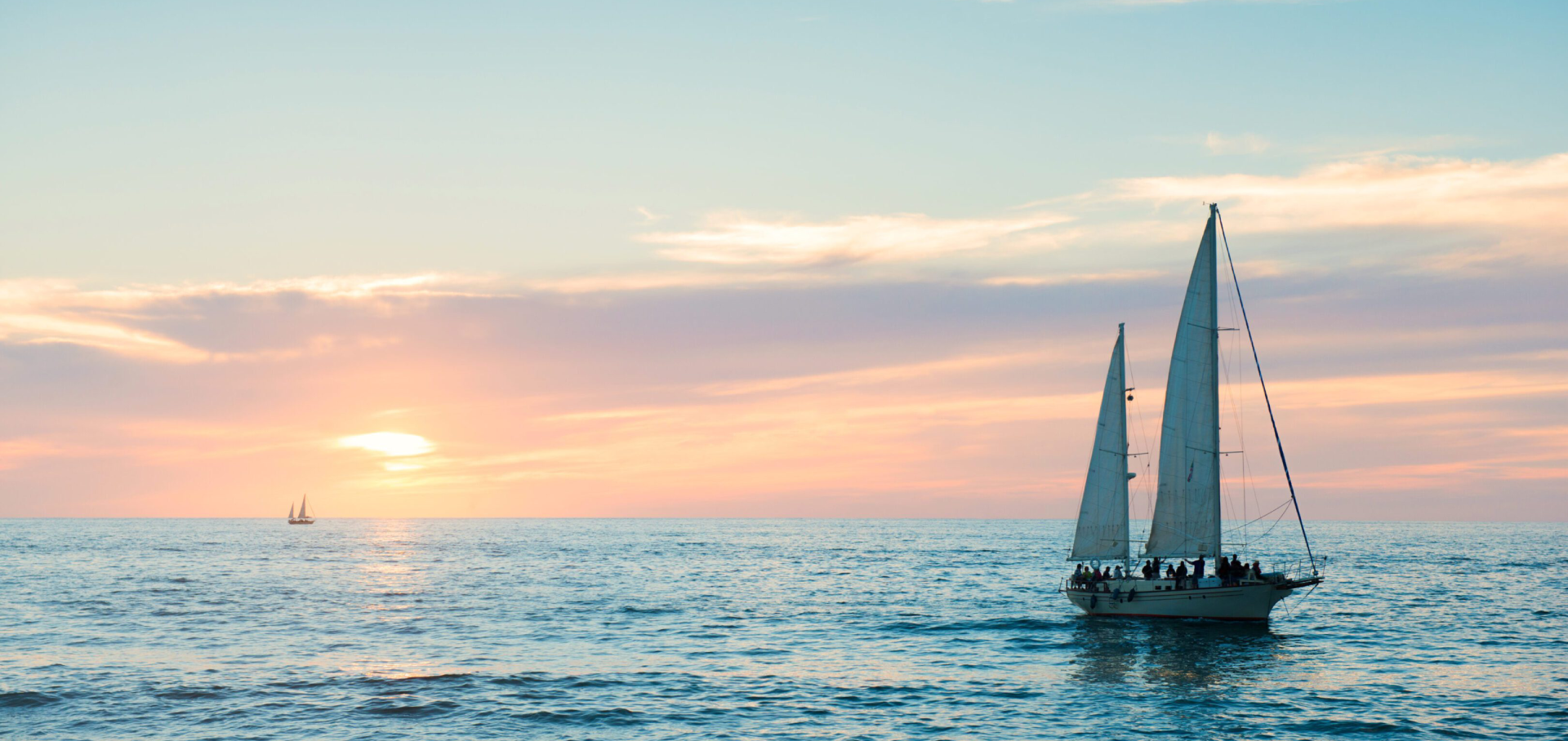 Sailboat gliding on calm ocean at sunset.