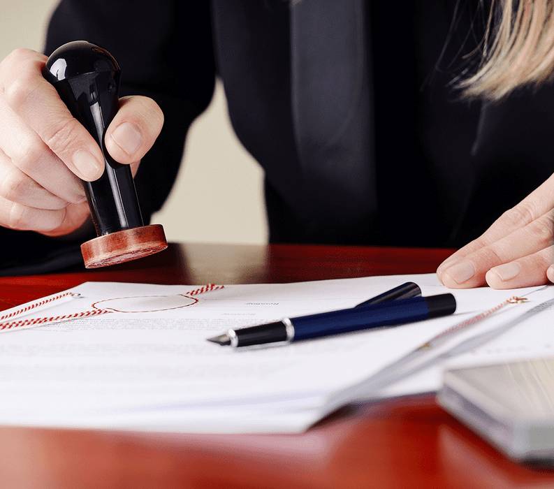 Person stamping an official document with a pen nearby.